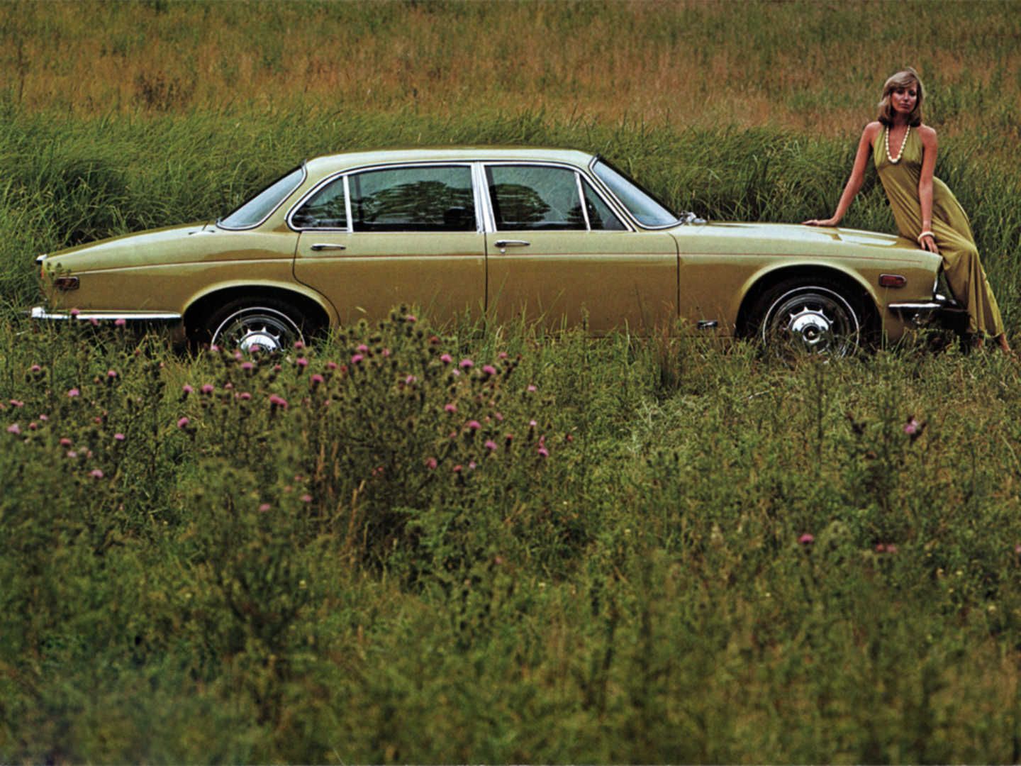 Jaguar XJ verte de profil dans un champ avec une femme sur le capot
