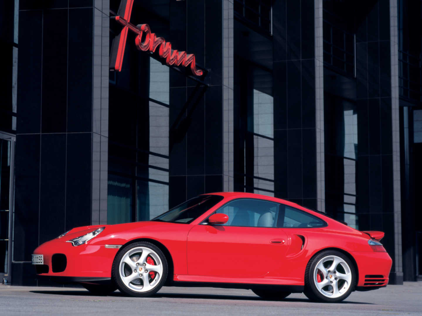 Porsche 911 "996" rouge vue de profil en bas d'un immeuble