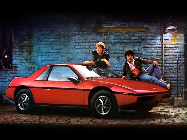 Pontiac Fiero rouge avec une personne sur le capot et une autre debout devant la porte conducteur