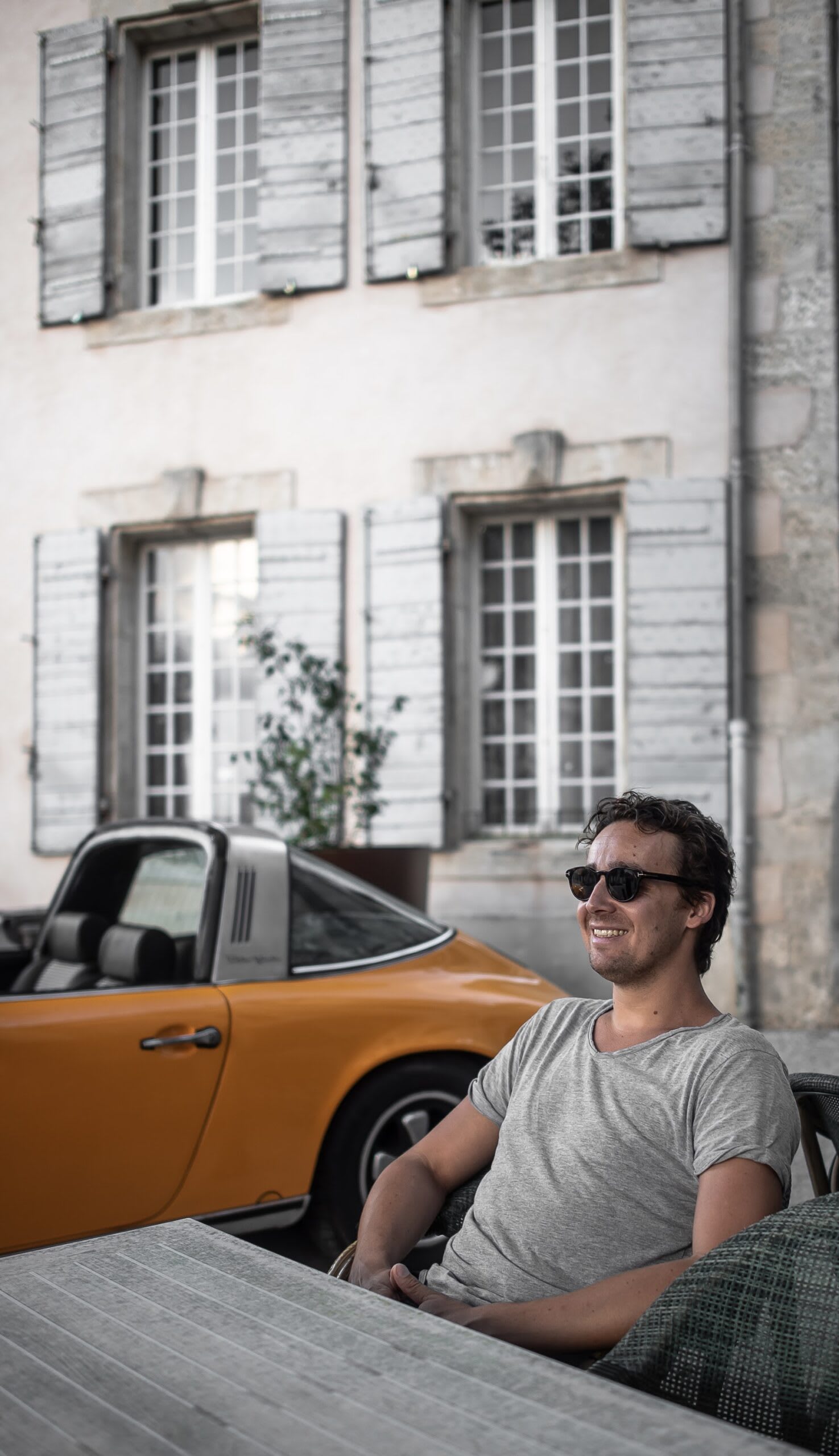 Vincent en terrasse avec sa Porsche en fond