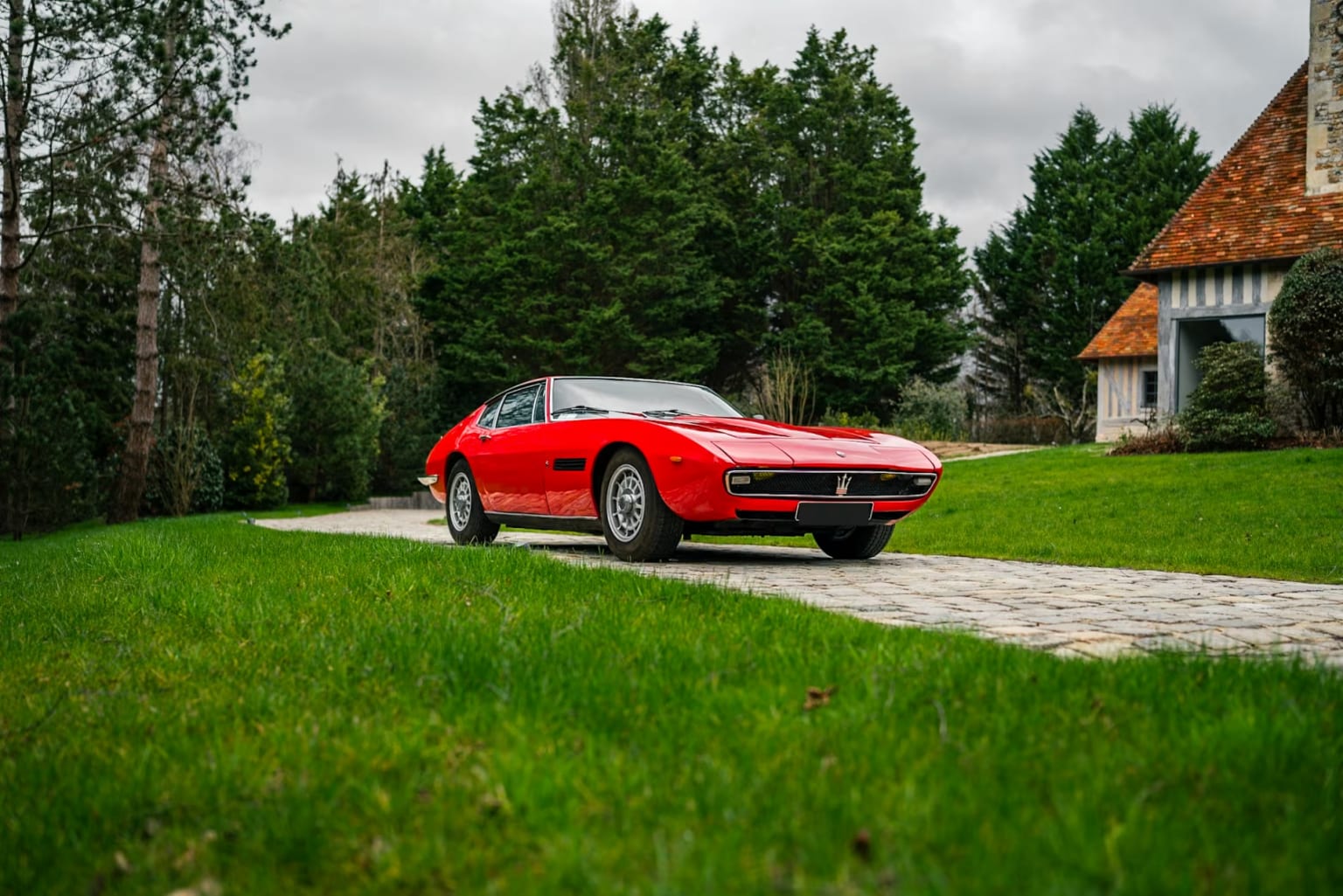 Maserati Ghibli rouge, garée sur un chemin en pierres entouré d'herbe.